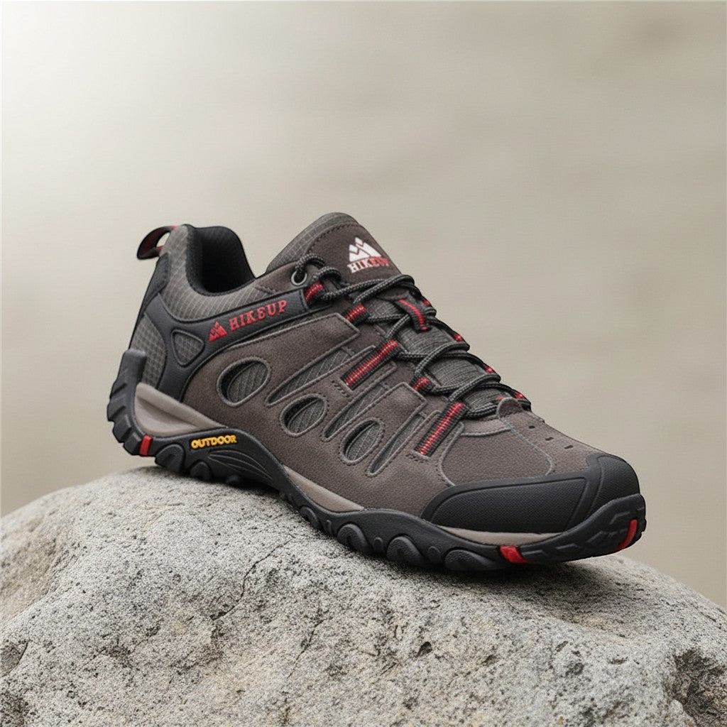 Chaussures de randonnée basses pour homme en gris anthracite avec détails rouges, posées sur un rocher. Ce modèle robuste est doté d’une semelle crantée assurant une bonne accroche et un bon maintien sur terrain accidenté.