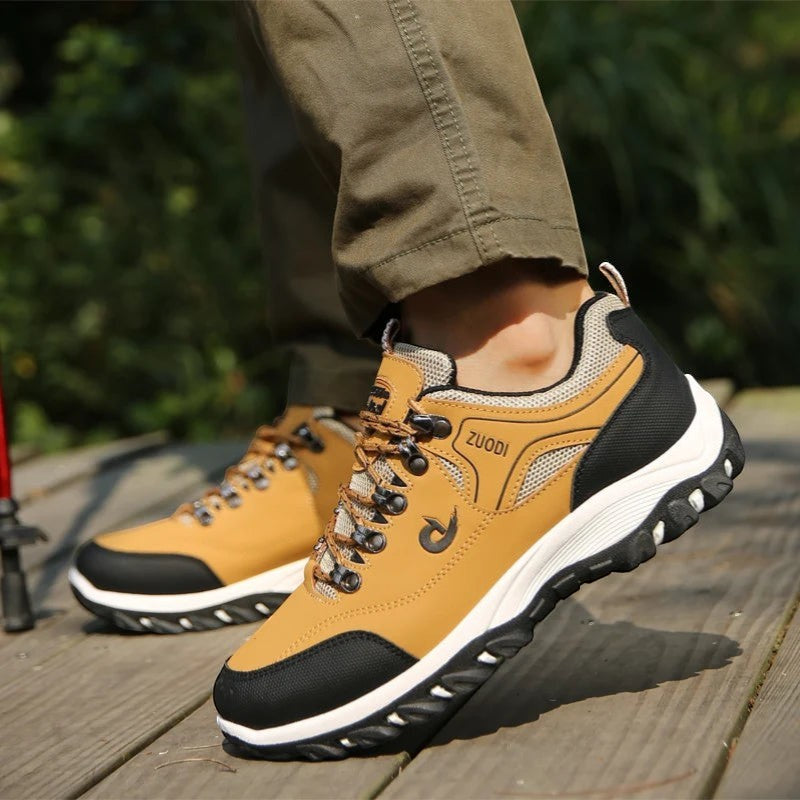 Chaussures de randonnée basses pour homme en beige portées en extérieur sur un rocher. Ce modèle offre une semelle crantée et un bon maintien pour une utilisation sur terrain irrégulier.