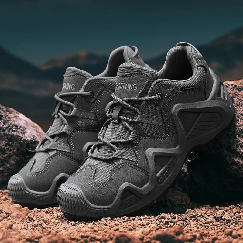 Paire de chaussures de randonnée basses pour homme en gris anthracite posées sur un terrain rocheux. Ce modèle offre une semelle crantée pour une bonne accroche et un bon maintien.