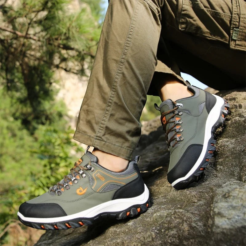 Chaussures de randonnée basses pour homme en gris portées sur un rocher en extérieur. Ce modèle dispose d’une semelle crantée offrant une bonne accroche sur terrain naturel.