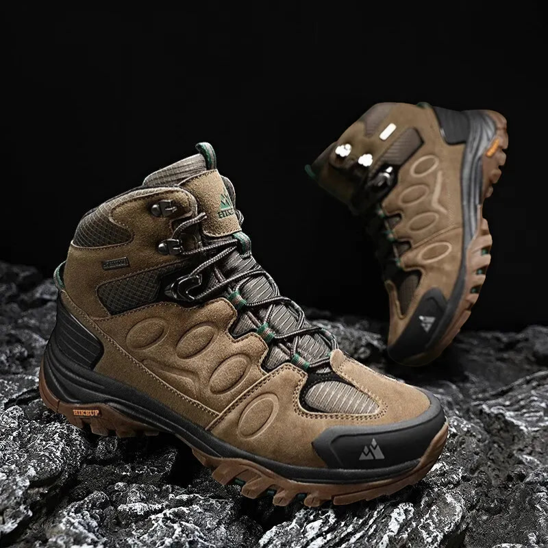 Chaussures de randonnée montantes pour homme en cuir suédé marron, présentées sur un sol rocheux avec une paire en arrière-plan. Ce modèle robuste est équipé d’une semelle crantée offrant une excellente accroche, avec des renforts à l’avant et un bon maintien de la cheville pour les terrains exigeants.