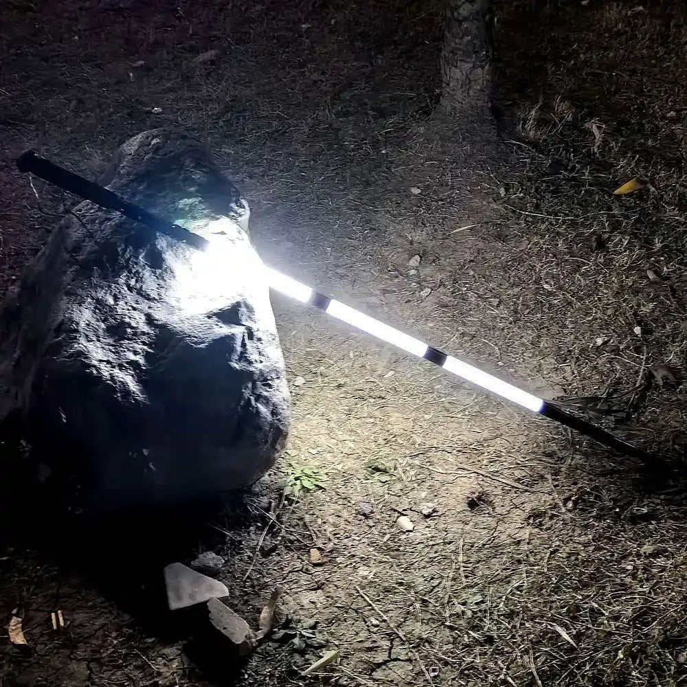 Bâton lumineux Passion Randonnée posé au sol de nuit près d’un rocher, éclairant une zone extérieure pour le camping ou la randonnée.